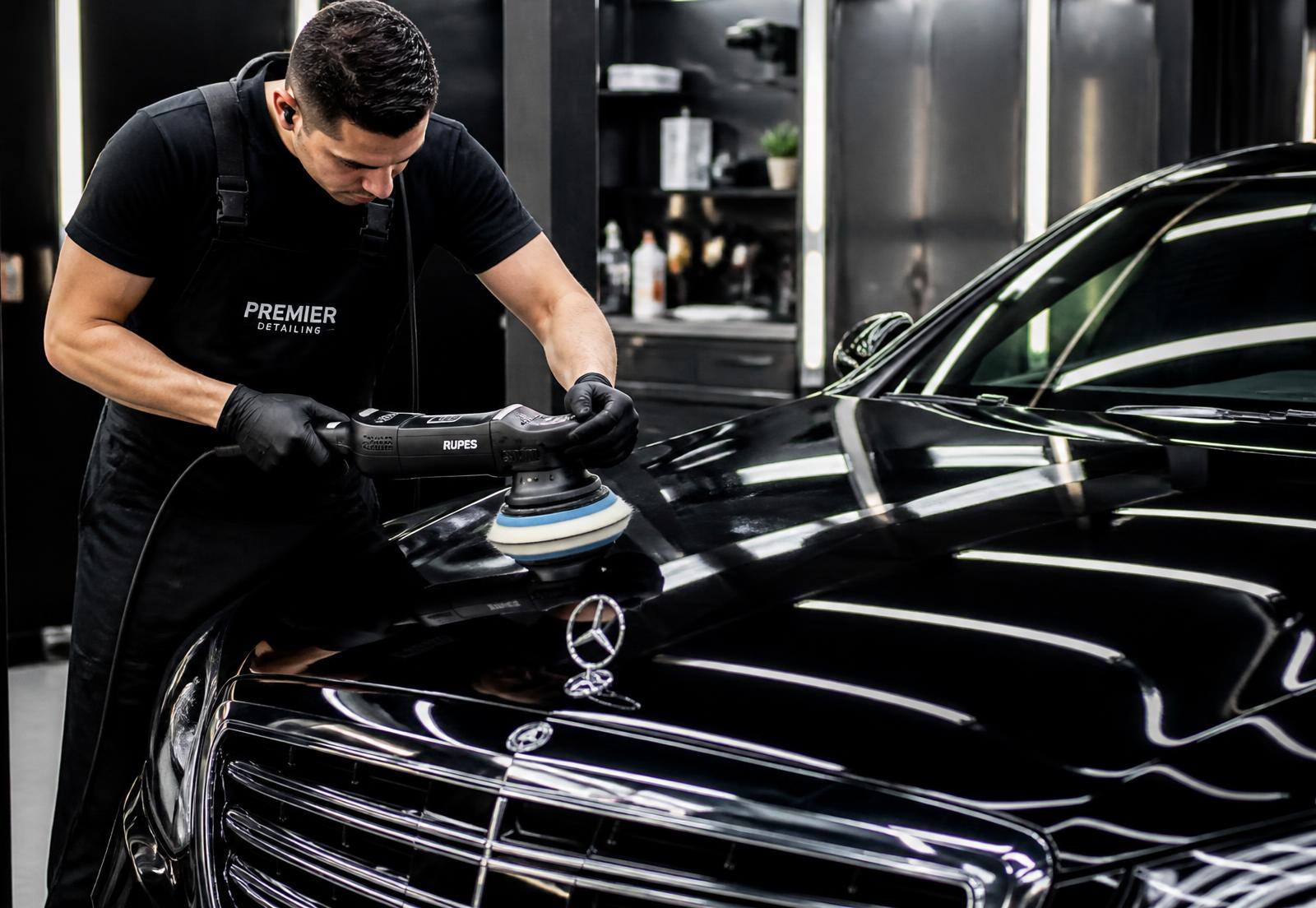 Detailer machine-polishing the hood of a glossy black luxury sedan